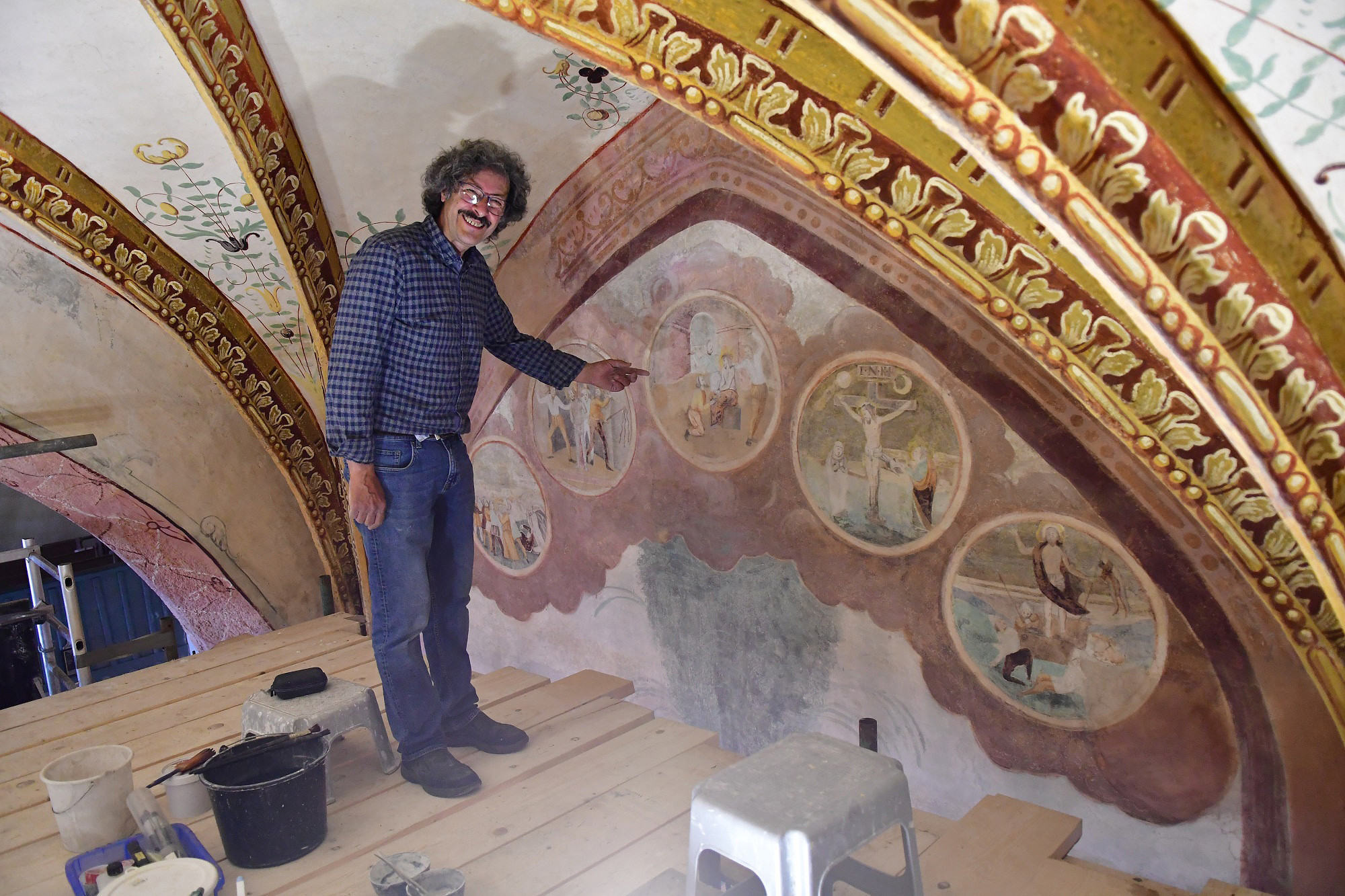 Während der Restaurierung steht der Restaurator am Gerüst und zeigt die Malereien.