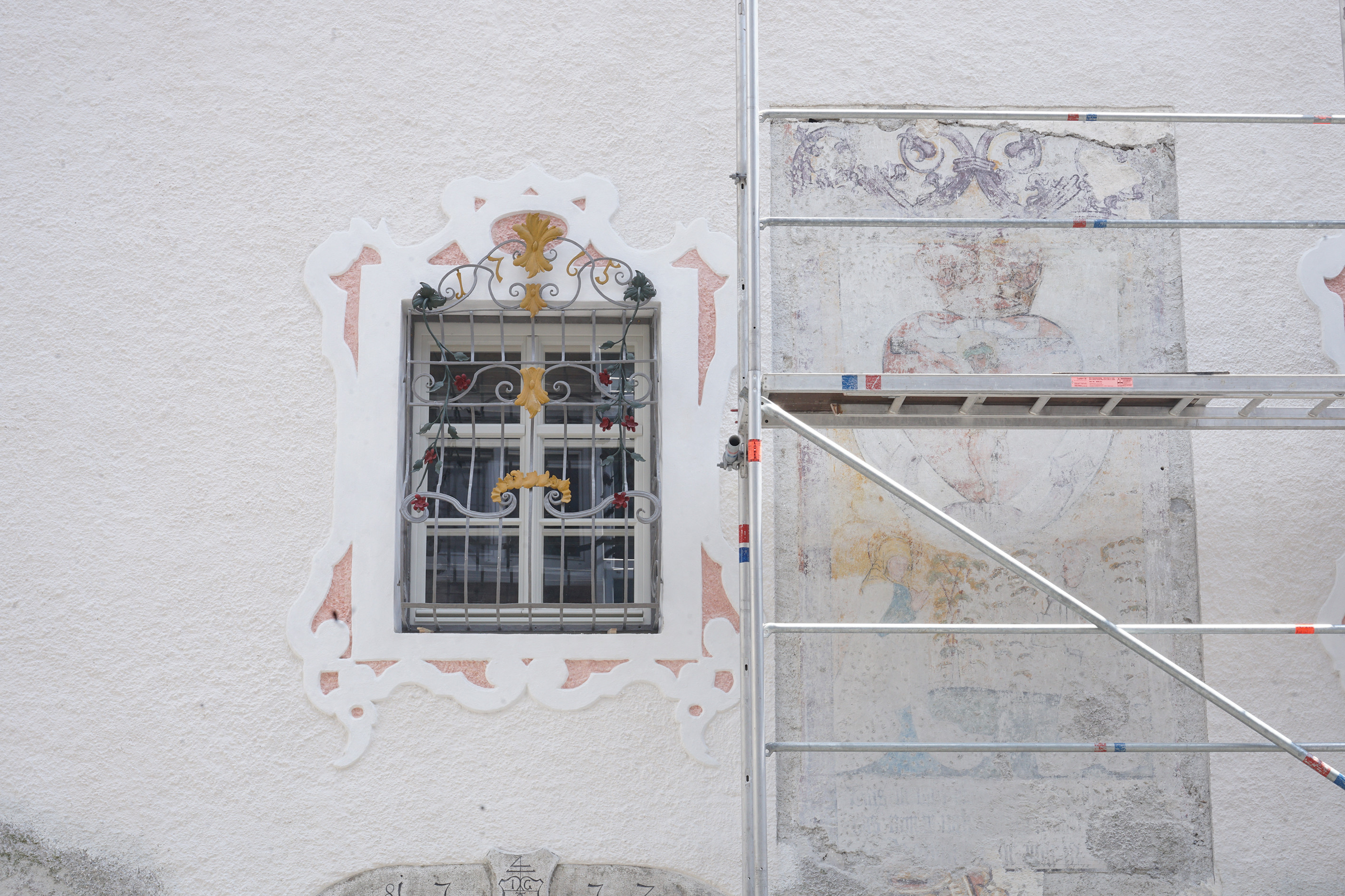Das Bild zeigt einen Ausschnitt der Westfassade mit Fenster und aufgedecktem gotischen Fresko.
