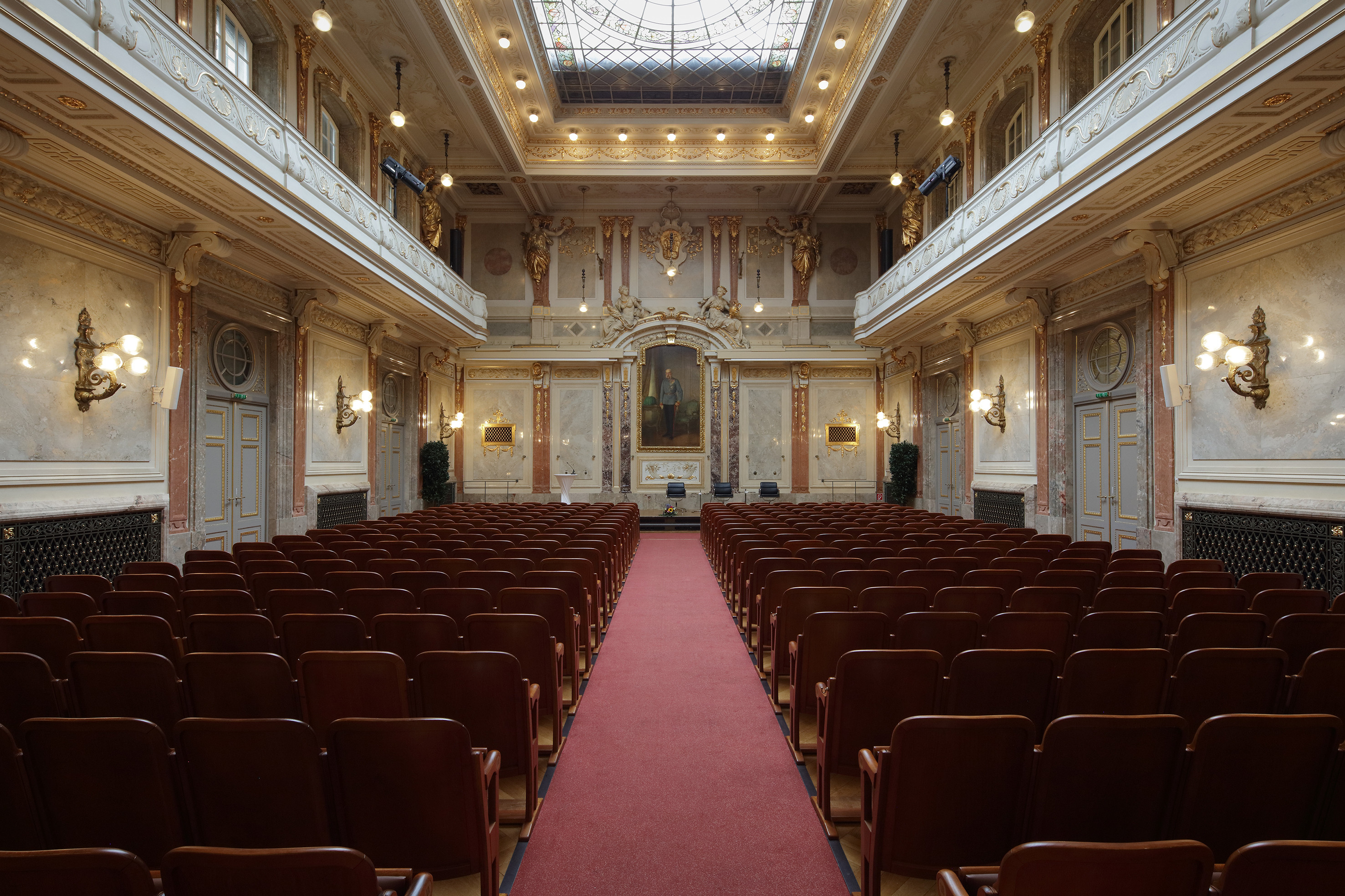 Großer Festsaal in brauner Theaterbestuhlung und Galerien an der Seite oben. Vorne die Marmorverkleidung mit Bild von Kaiser Franz Josef